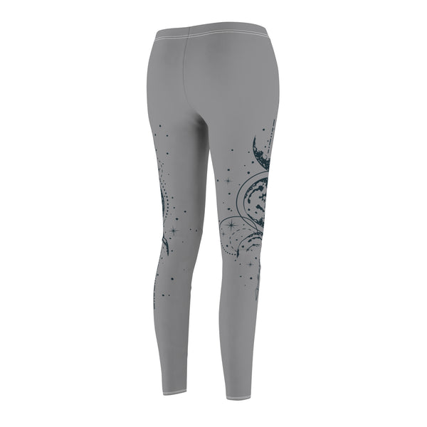 Rear view of gray leggings featuring a vertical hand-drawn illustration of moon phases and geometric arrows on the left leg. The fabric has a soft, brushed suede texture with visible white stitching at the waist and hem.
