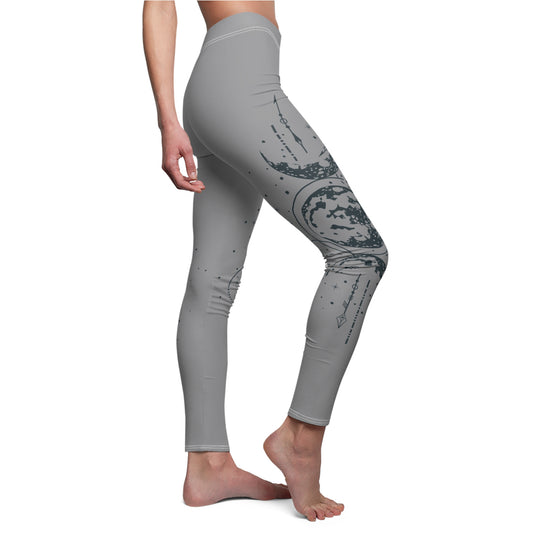 Right side view of gray leggings featuring a vertical hand-drawn illustration of moon phases and geometric arrows on the left leg. The fabric has a soft, brushed suede texture with visible white stitching at the waist and hem.