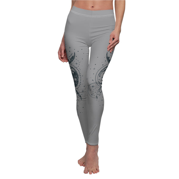 Front view of gray leggings featuring a vertical hand-drawn illustration of moon phases and geometric arrows on the left leg. The fabric has a soft, brushed suede texture with visible white stitching at the waist and hem.
